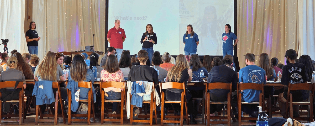 cincinnati animal care's annual all staff meeting showing the backs of staff looking up to four director on stage giving a presentation