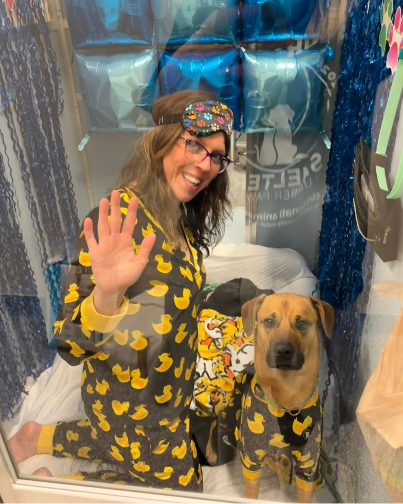 woman and dog in matching pjs inside dog kennel during shelter slumber pawty