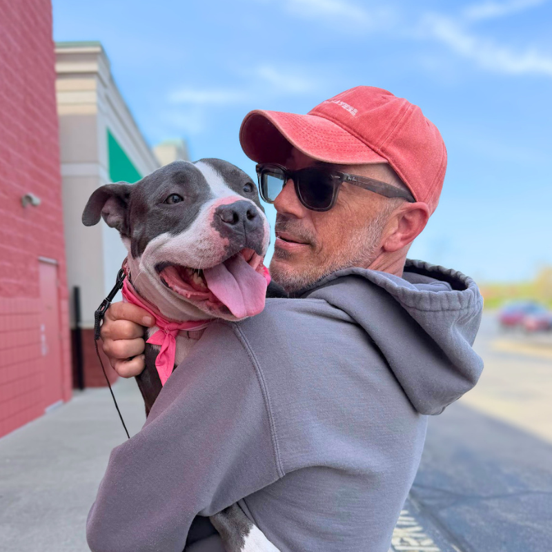 man holding a smiling grey and white dog close to his chest