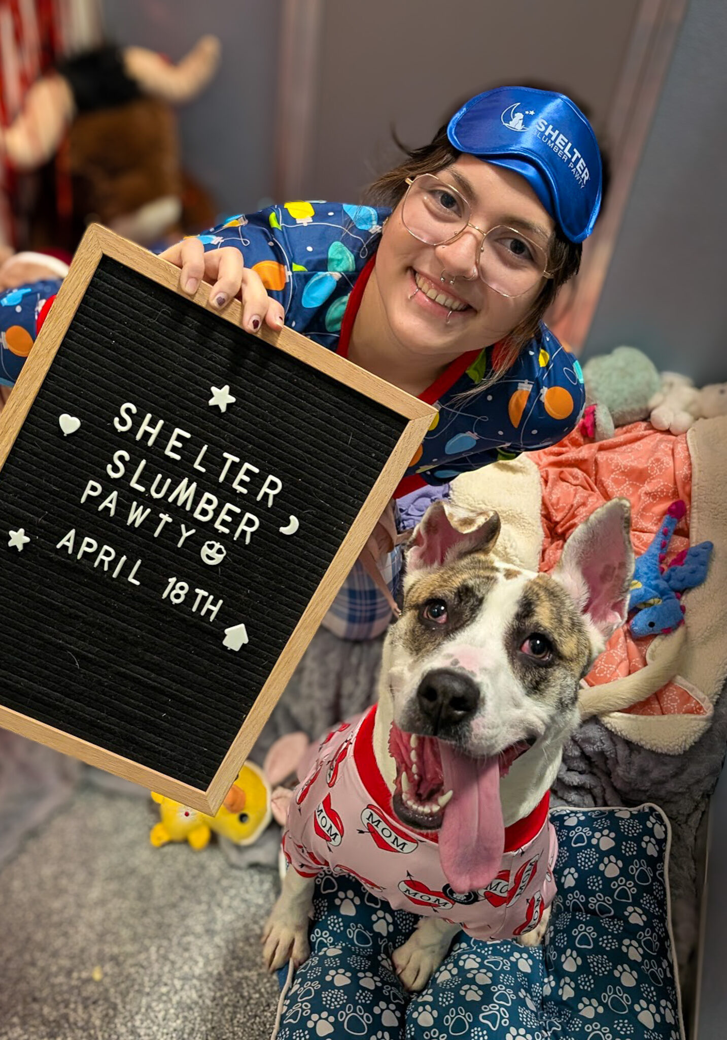 woman and dog sitting and smiling inside shelter dog kennel surrounded by blankets pillows and stuffed animals